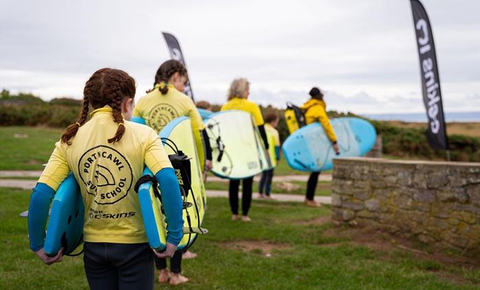 Image of students and their instructor carrying surf boards as they head towards their lesson location